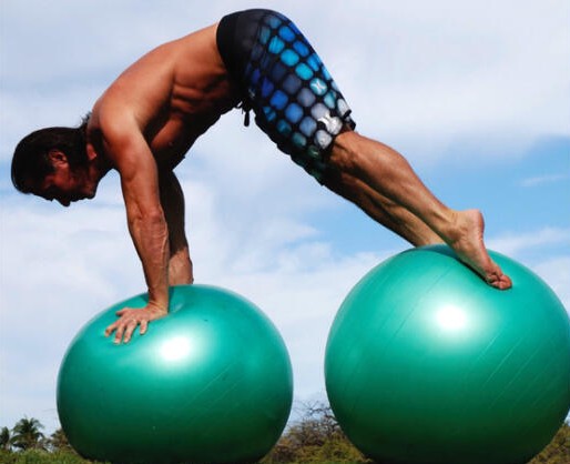 Scott Aloha holding a pike, hands on one green stability ball and feet on another, under a blue sky